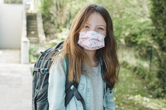 School-age girl wearing a face mask and backpack before school