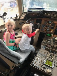 A young blond girl and boy sit in the cockpit of a plane
