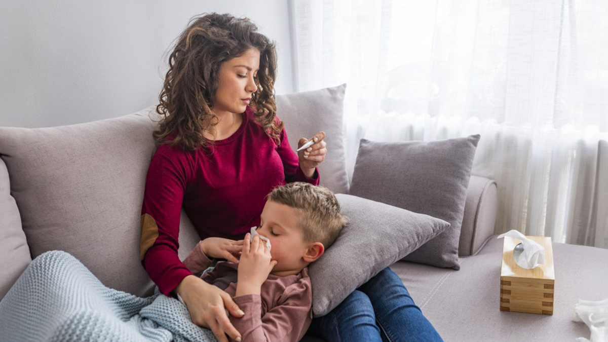 Mom taking her son's temperature while he blows his nose into a tissue